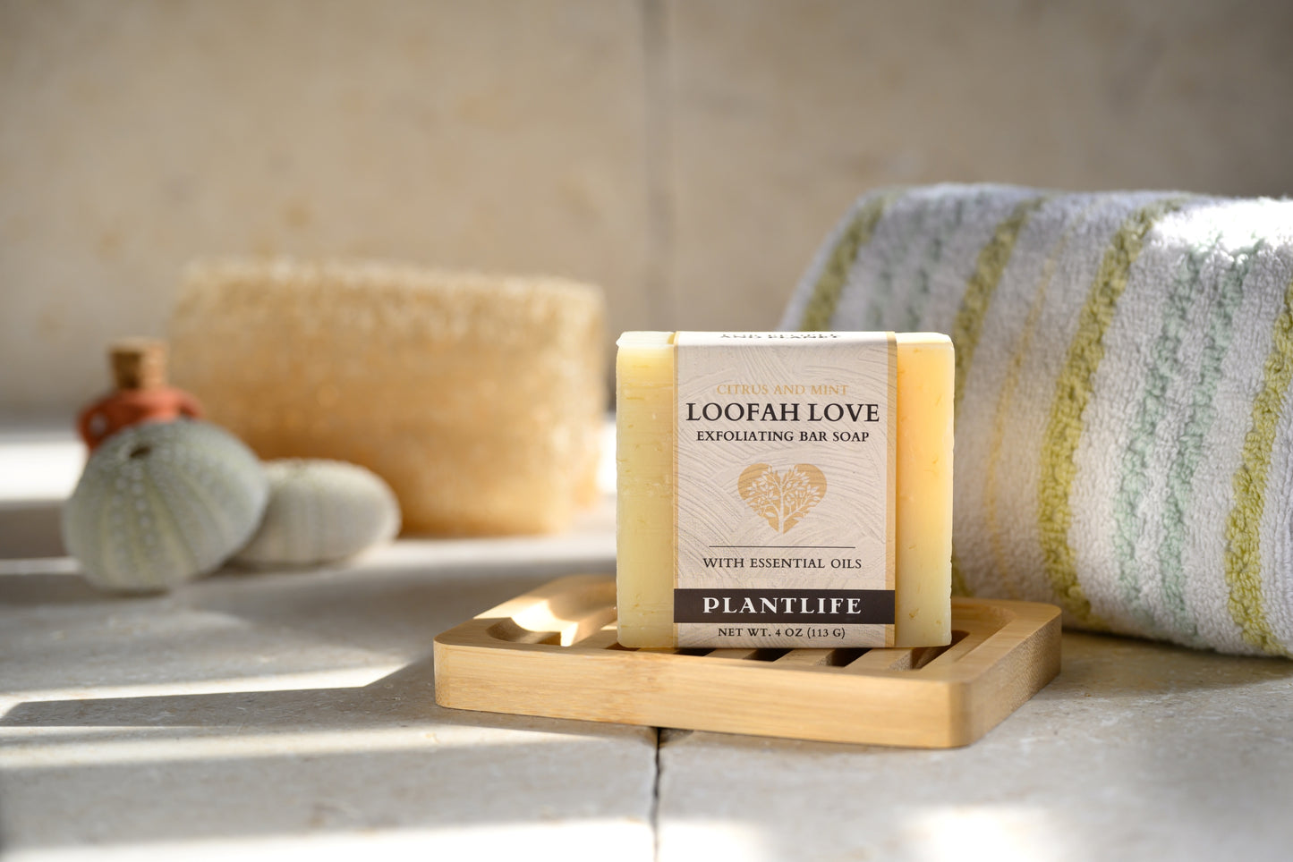 Bar of soap on a wooden tray with a towel and bath products in the background