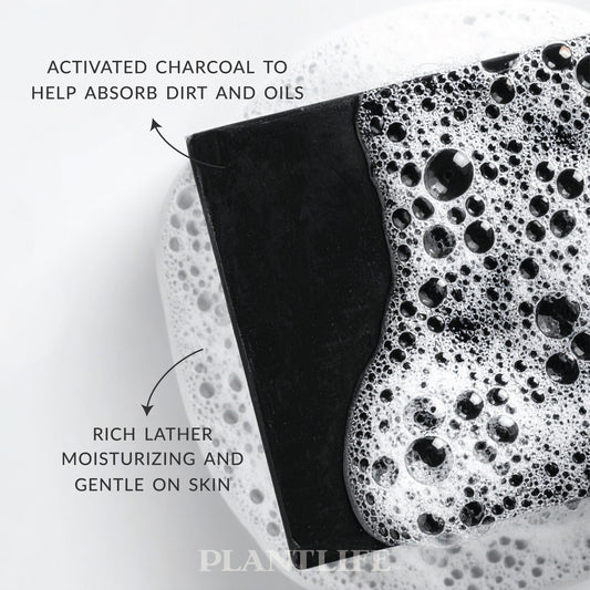 Close-up of a black Plantlife soap bar resting in foamy water. Text on the image highlights “Activated charcoal to help absorb dirt and oils” and “Rich lather, moisturizing and gentle on skin.”