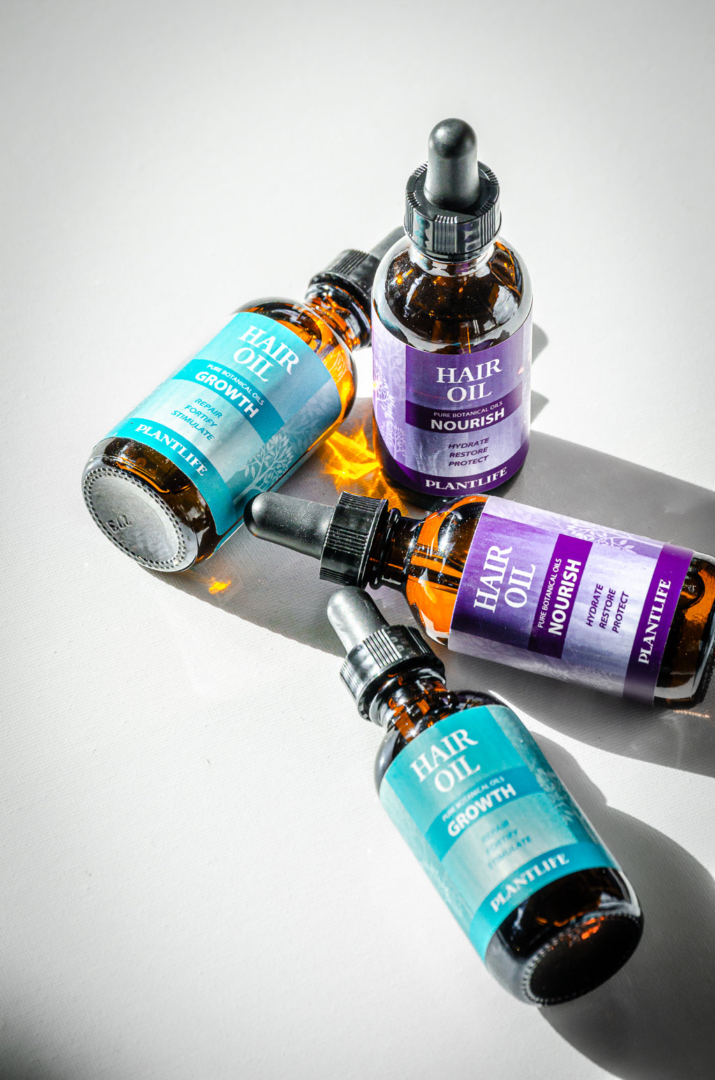 Plantlife Hair Oils in Growth and Nourish formulas shown with glass droppers on a white surface in natural light.