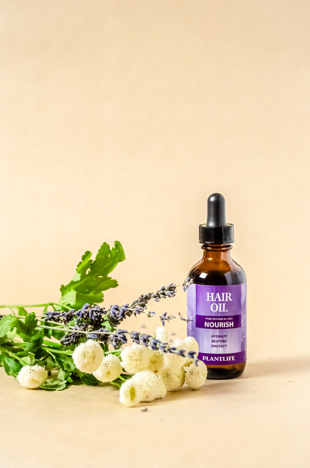 Plantlife Nourish Hair Oil bottle surrounded by fresh lavender and chamomile on a beige background.