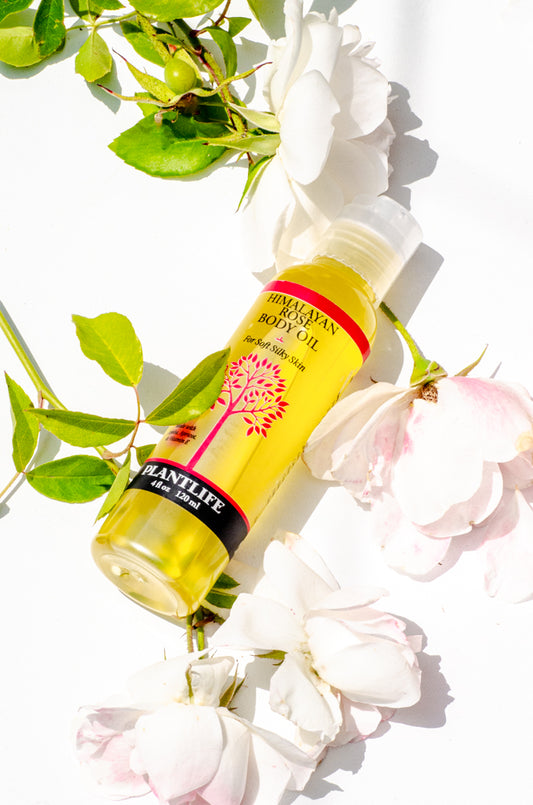 Yellow bottle of plant-based body oil with green leaves and white flowers on a white background