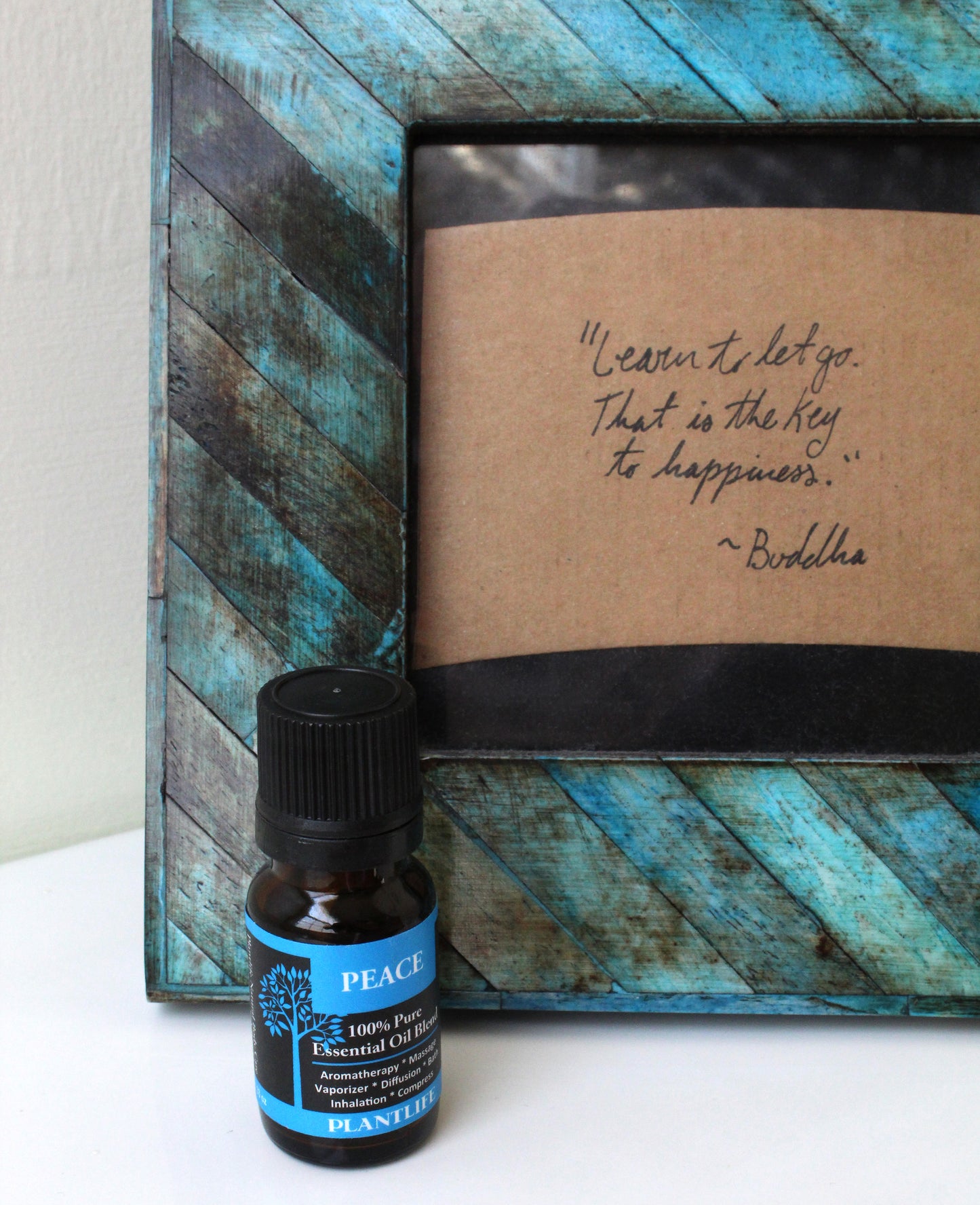 Bottle of 'Peace' essential oil with a wooden frame containing a quote on a white surface