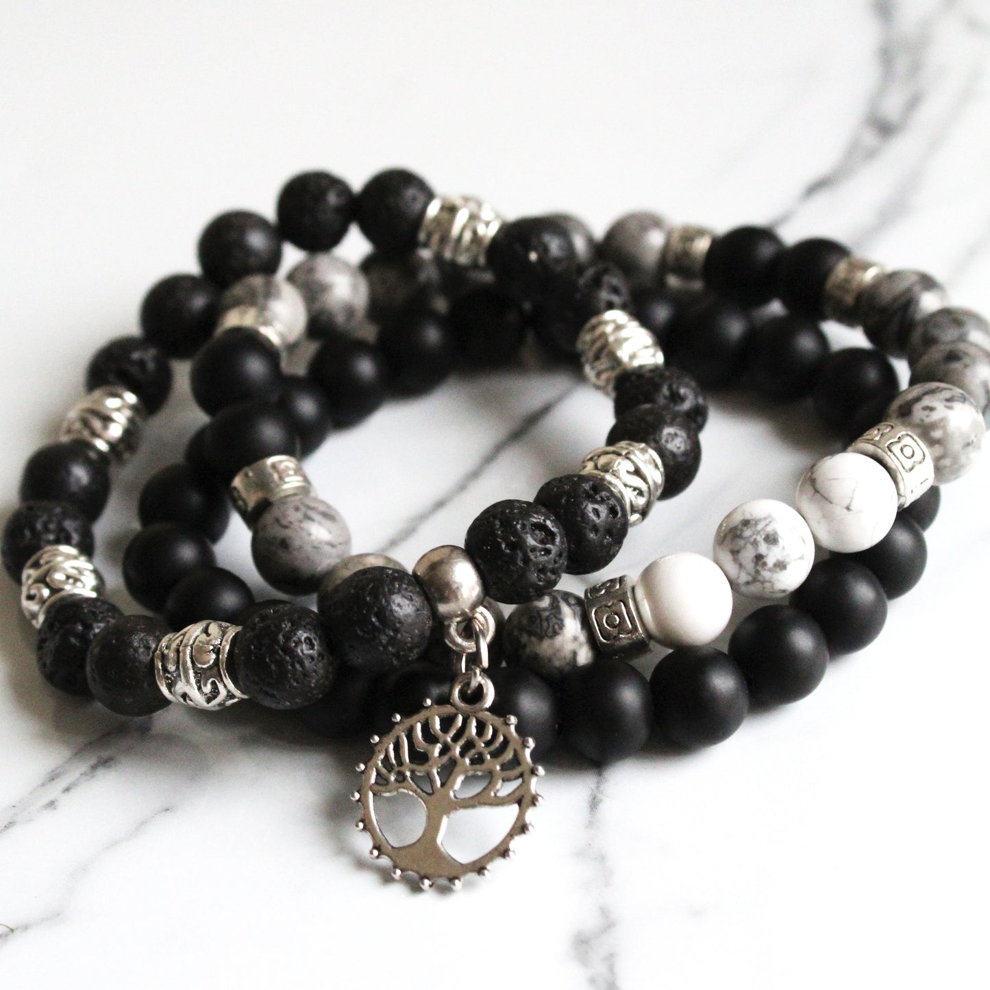 Stack of black, white, and gray beaded bracelets with tree of life charm on a marble surface