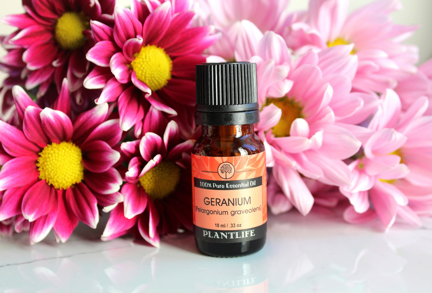 Bottle of Plantlife Geranium essential oil with pink flowers in the background