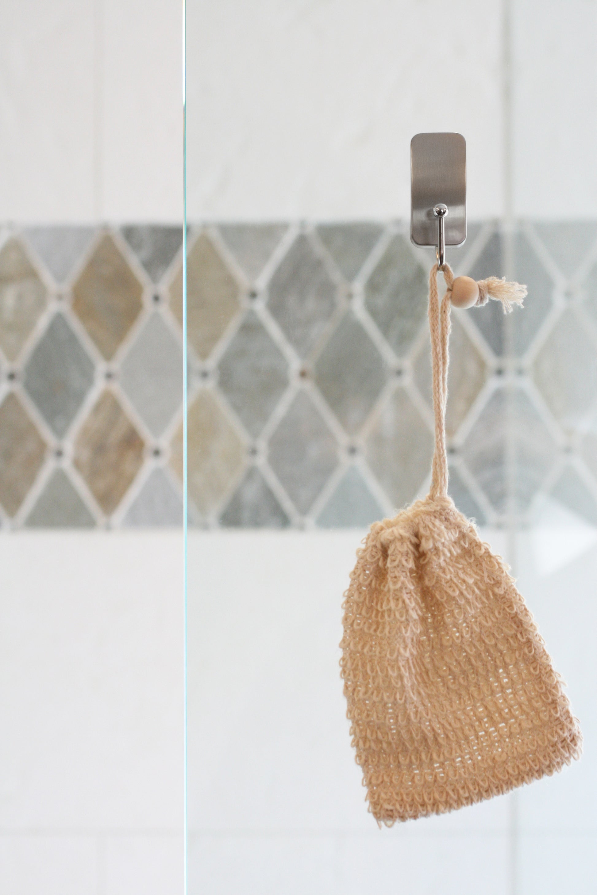 Plantlife natural soap saver sack hanging in shower on glass hook with tile background