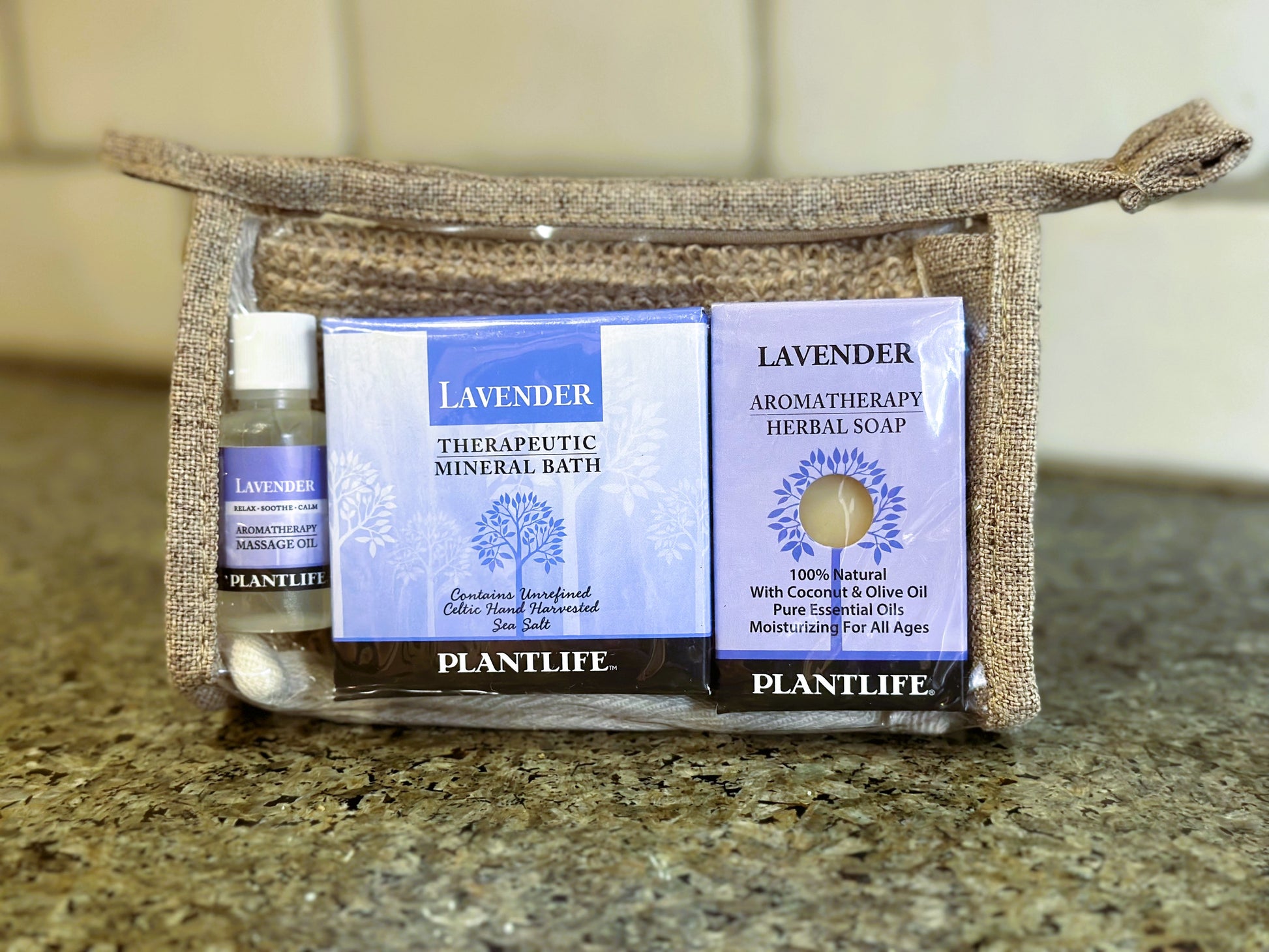 Plantlife Lavender gift set in a woven pouch with therapeutic mineral bath, aromatherapy herbal soap, and massage oil on a countertop