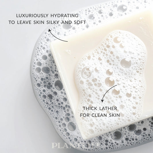 Plantlife bar soap shown on a bed of foamy bubbles, featuring a creamy white color with thick, airy lather. Text highlights its luxuriously hydrating formula designed to leave skin silky and soft, with rich lather for a clean, gentle wash.