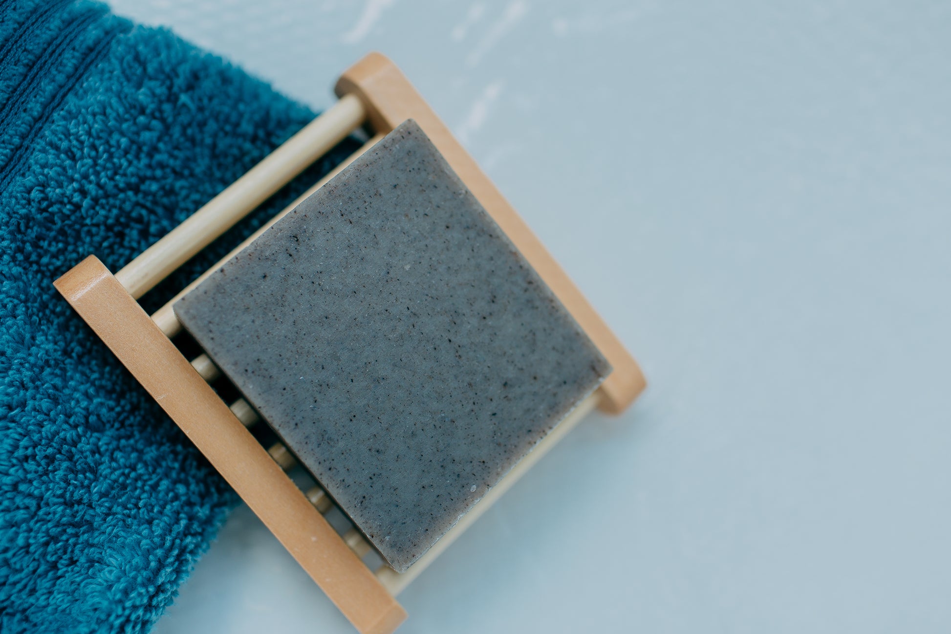 Plantlife black soap with activated charcoal on wooden soap dish next to blue towel in bathroom setting