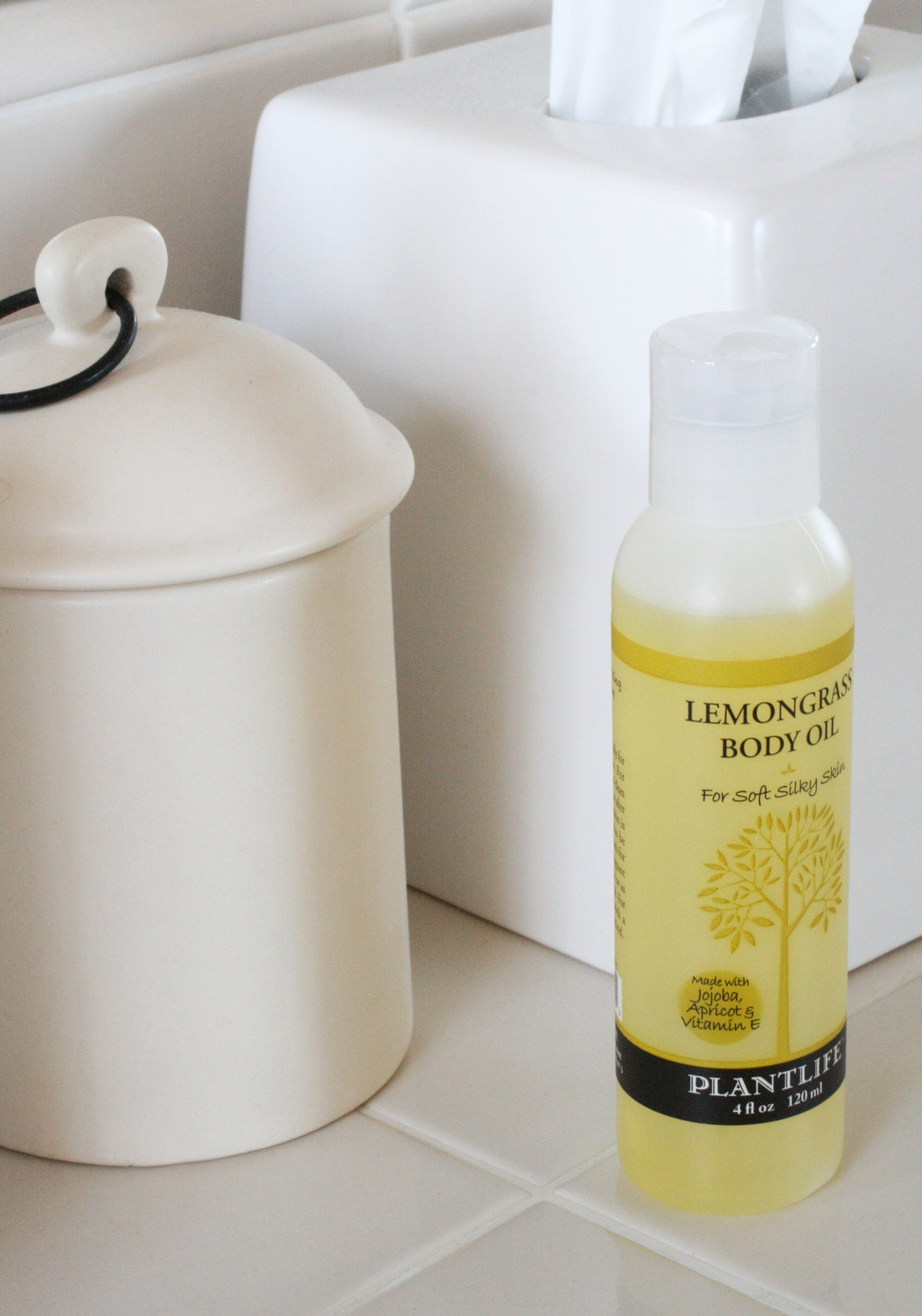 Bottle of Plantlife Lemongrass Body Oil on a bathroom counter next to a white container.
