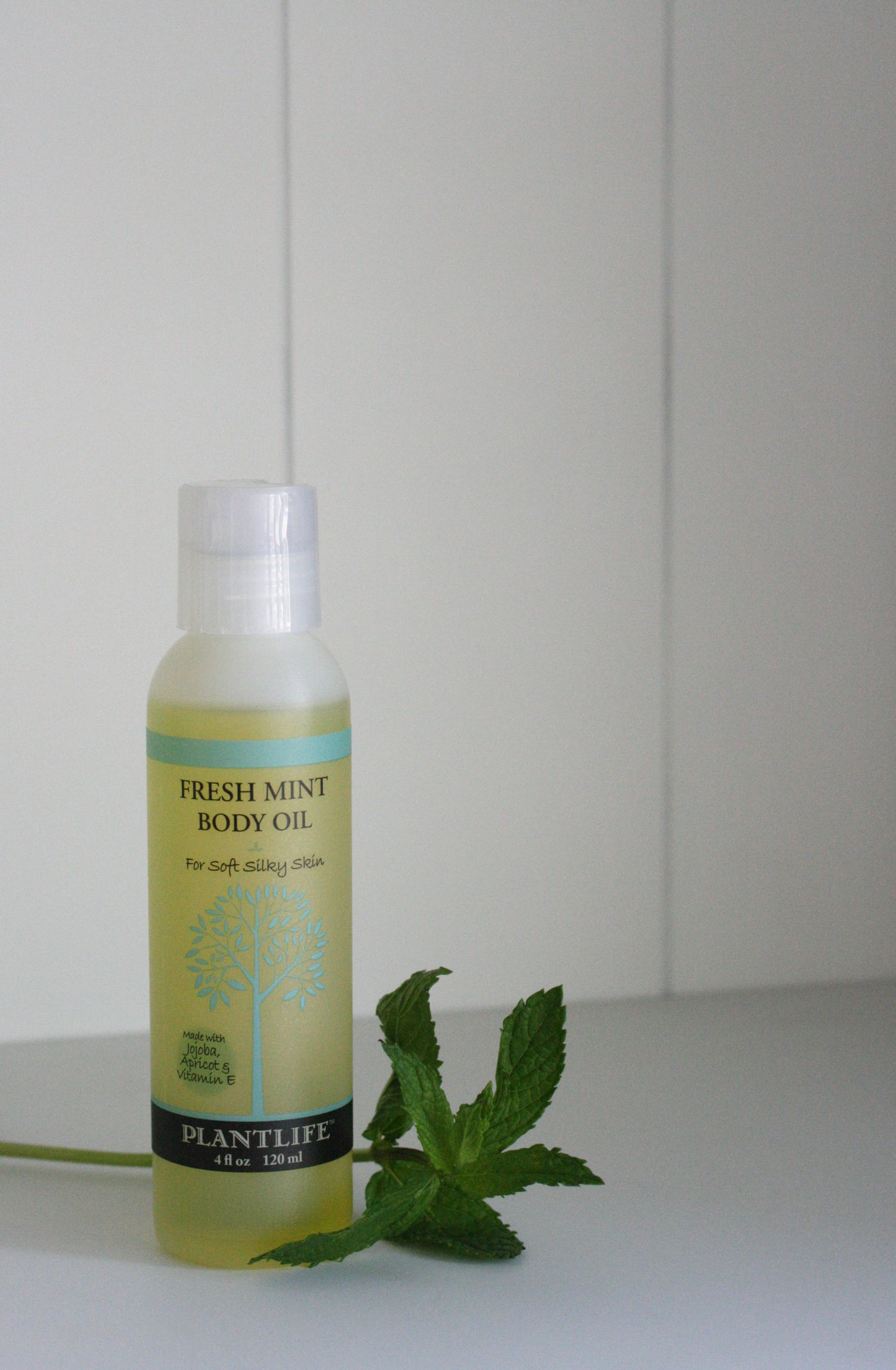 Bottle of fresh mint body oil with a plantain leaf on a white surface
