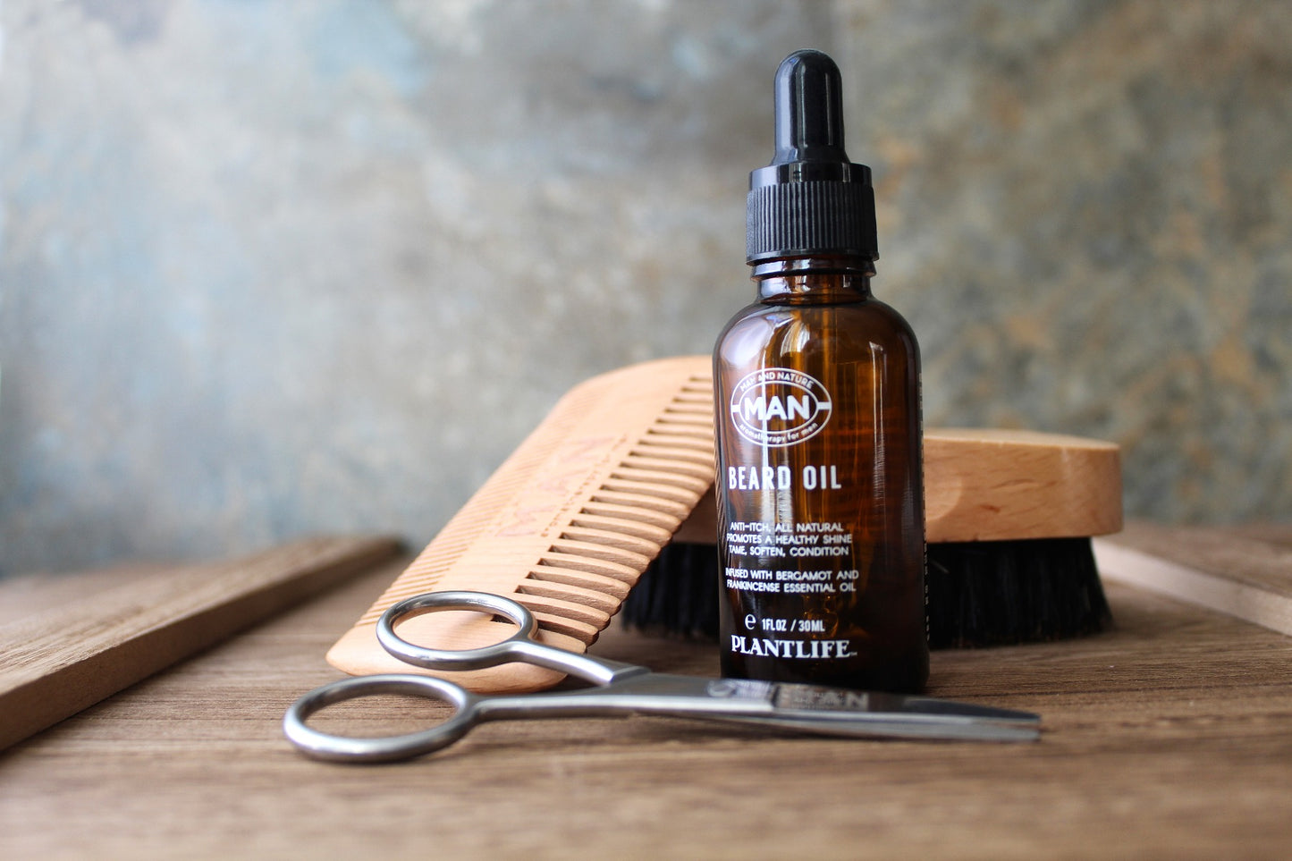 Plantlife Beard Oil bottle with dropper, wooden comb, trimming scissors, and brush on a wooden surface.