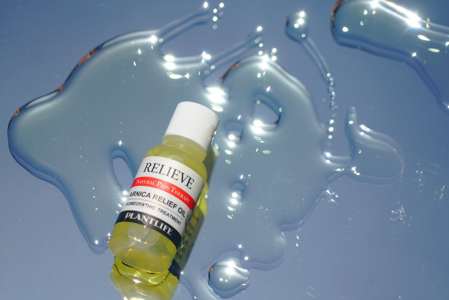 Plantlife Arnica Relief Oil bottle on a reflective surface with spilled oil, showcasing the natural pain therapy product’s texture and light-catching appearance for promotional use.