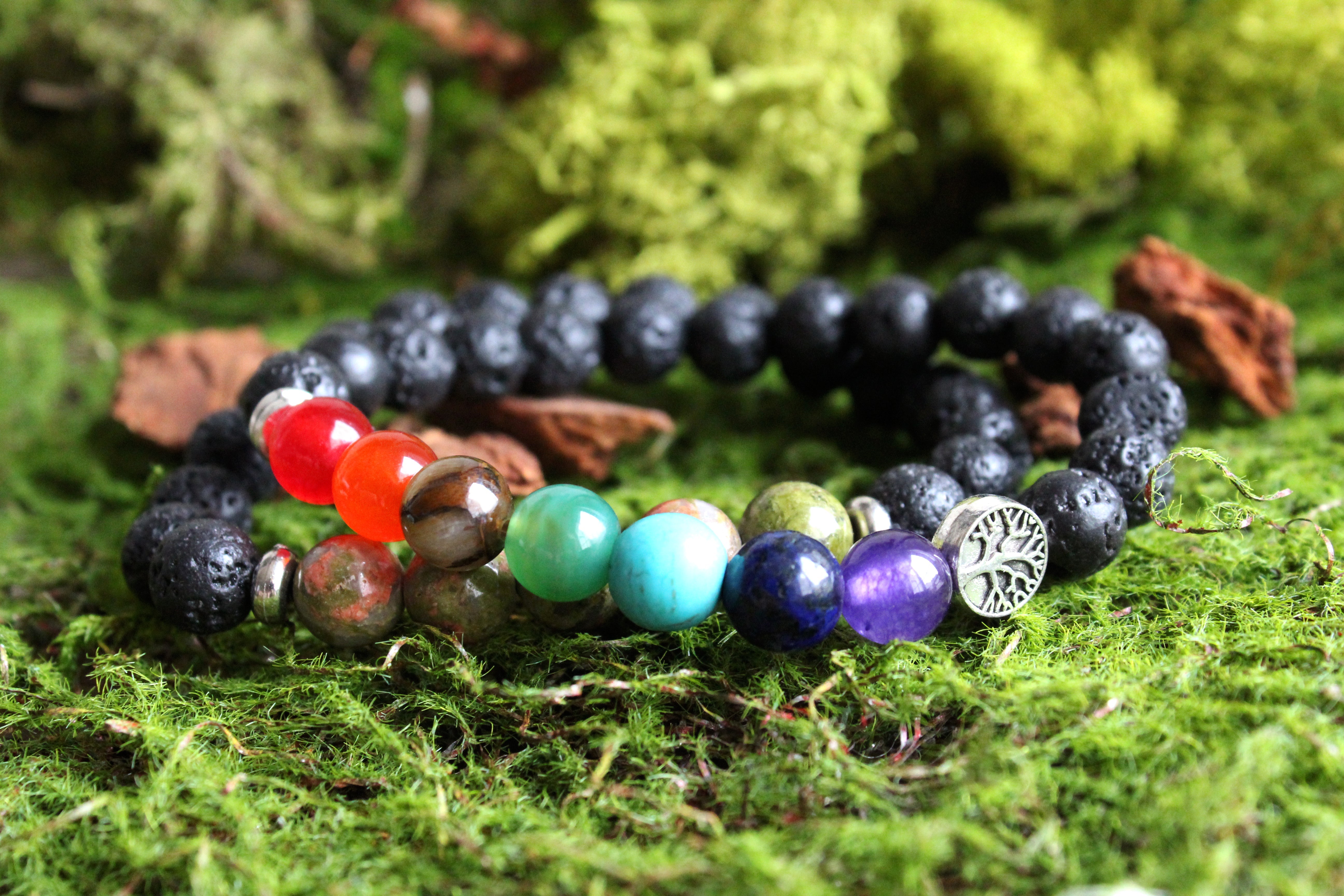 Lava stone aromatherapy bracelets with colorful beads and a tree charm resting on green moss.