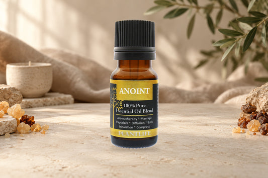 Plantlife Anoint Essential Oil Blend bottle on a stone surface with resin, linen, and soft greenery.