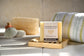 Bar of soap on a wooden tray with a towel and bath products in the background