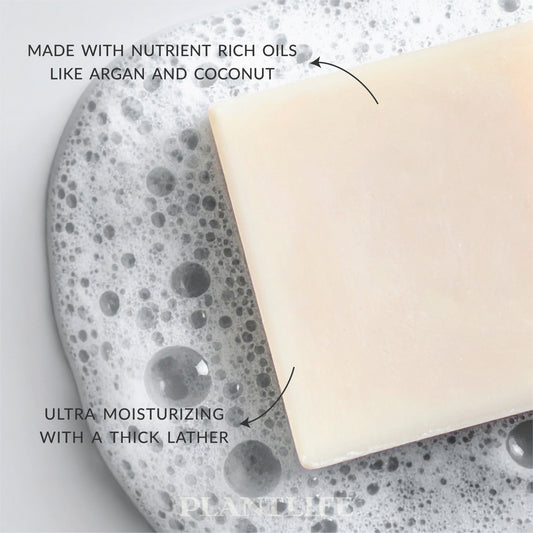 Close-up of a creamy white Plantlife soap bar resting in foamy water. Text on the image reads “Made with nutrient-rich oils like argan and coconut” and “Ultra moisturizing with a thick lather.”