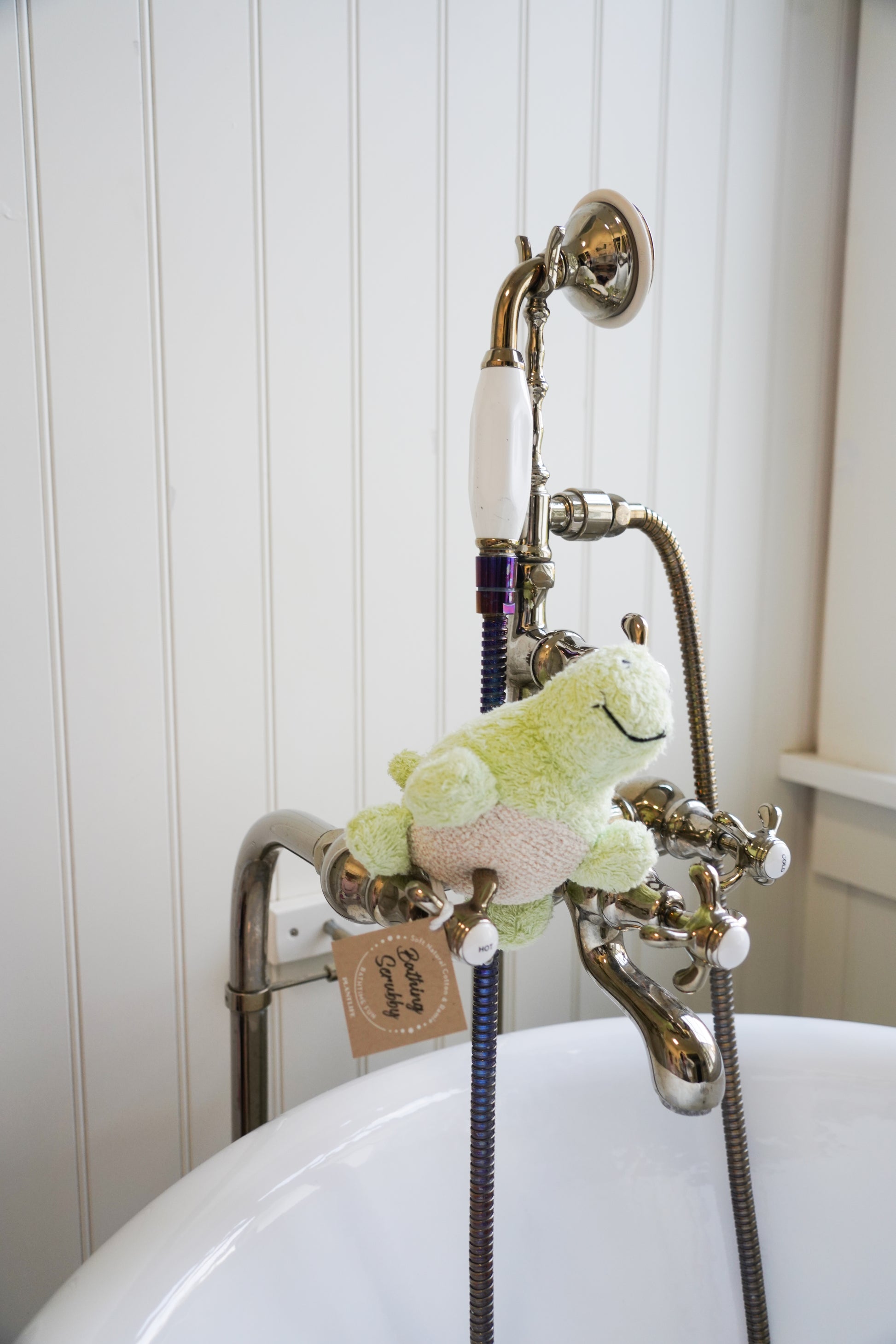 Plush toy attached to a shower head with a white bathtub in the background