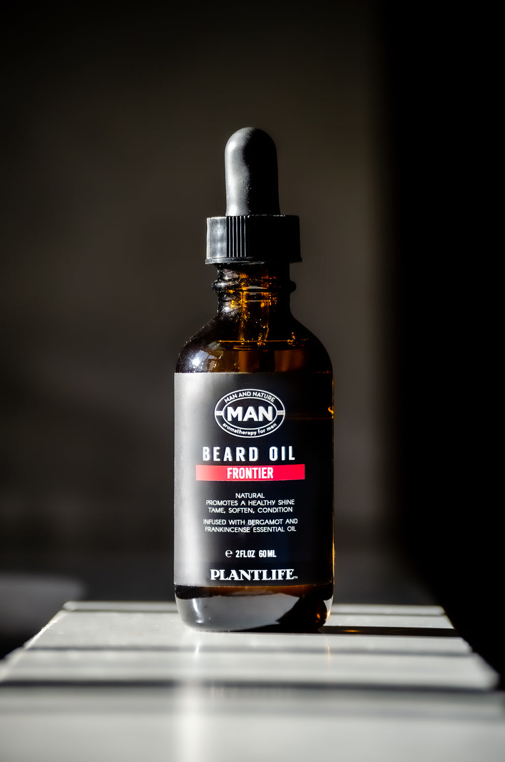 Plantlife Frontier Beard Oil 2 oz amber glass dropper bottle with bergamot and frankincense essential oils on a dark background