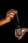 Plantlife Frontier Beard Oil 2 oz bottle held in hand with glass dropper dispensing beard oil against a dark background