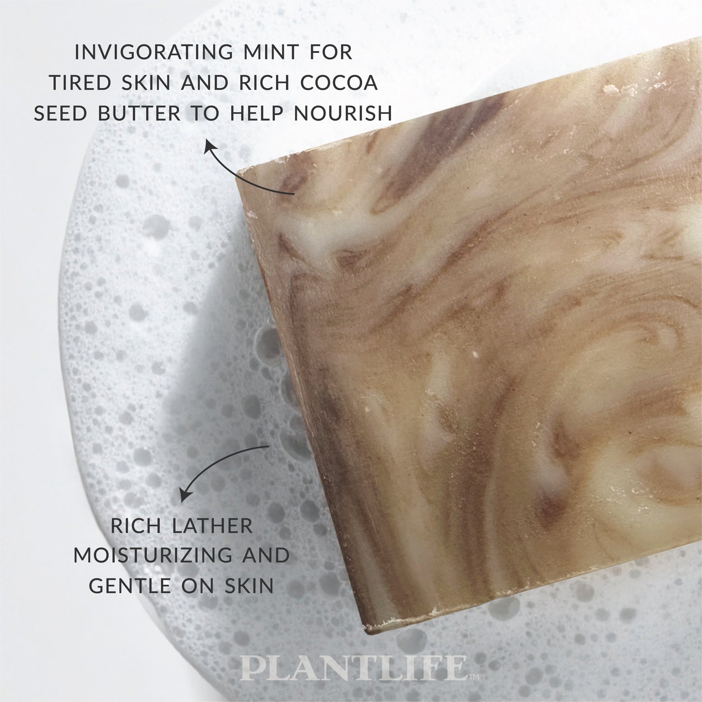 Close-up of a brown and cream swirled Plantlife soap bar resting in bubbly water. Text on the image highlights “Invigorating mint for tired skin and rich cocoa seed butter to help nourish” and “Rich lather, moisturizing and gentle on skin.”