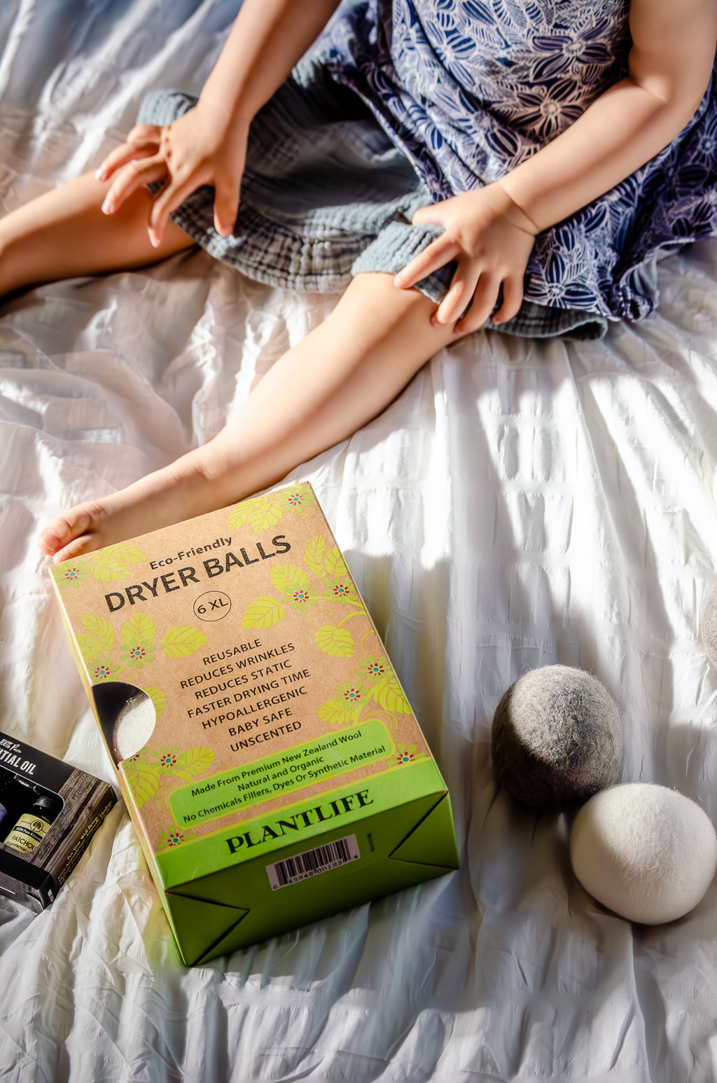 Box of Plantlife dryer balls on a bed with a person sitting nearby.