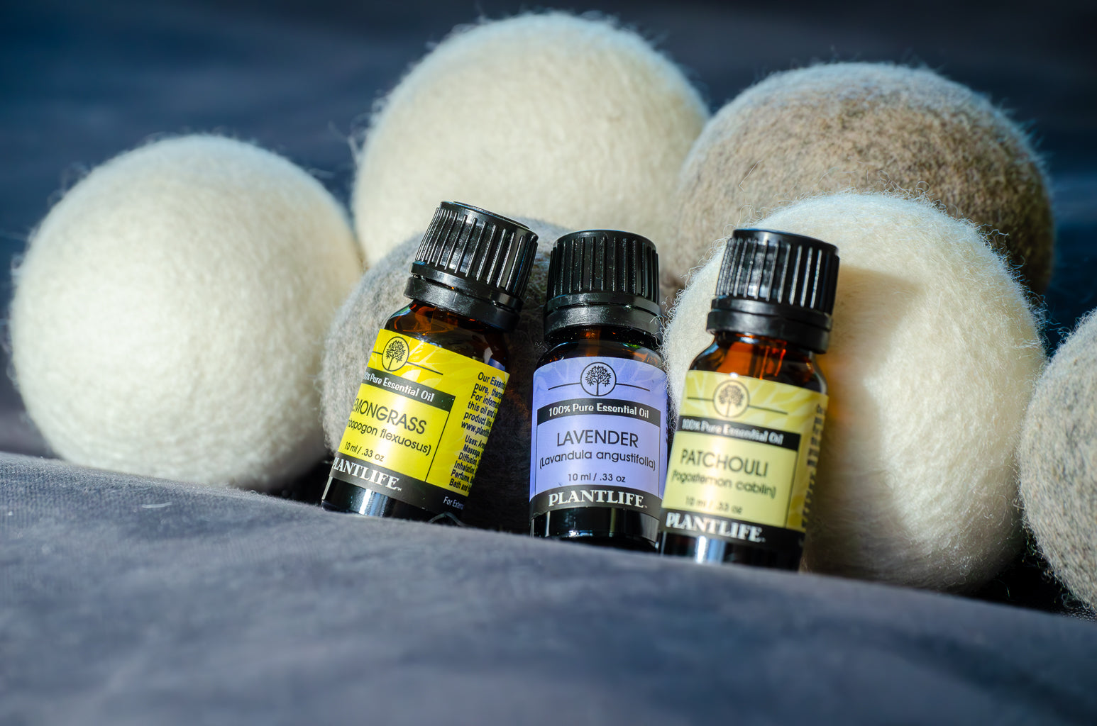 Three small bottles of Plantlife essential oils with wool dryer balls on a dark background