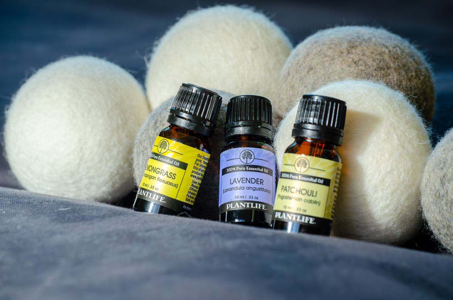 Three small bottles of Plantlife essential oils with wool dryer balls on a dark background