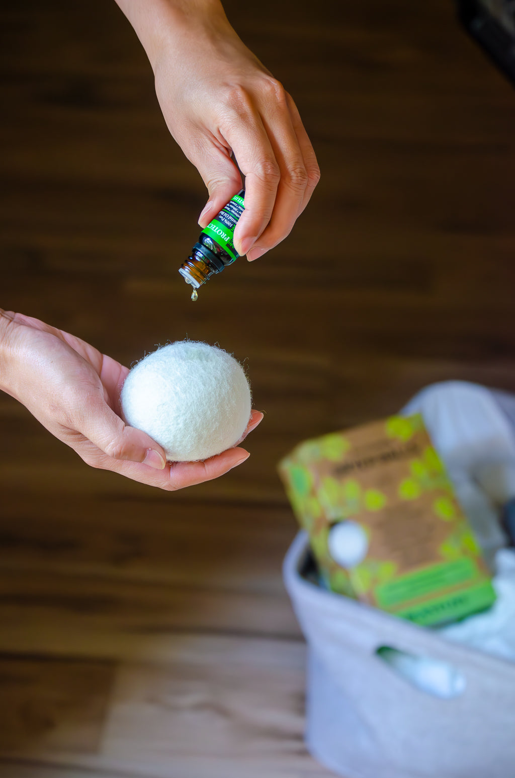 Person holding a white bath bomb with a bottle of essential oil over a wooden surface.
