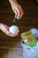 Person holding a white bath bomb with a bottle of essential oil over a wooden surface.