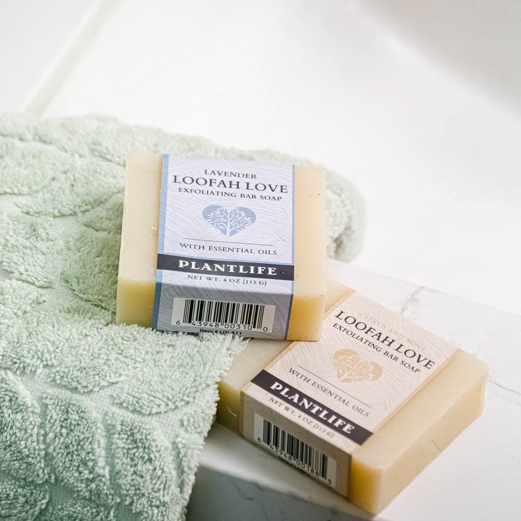 Two bars of Plantlife soap on a white surface with a green towel.