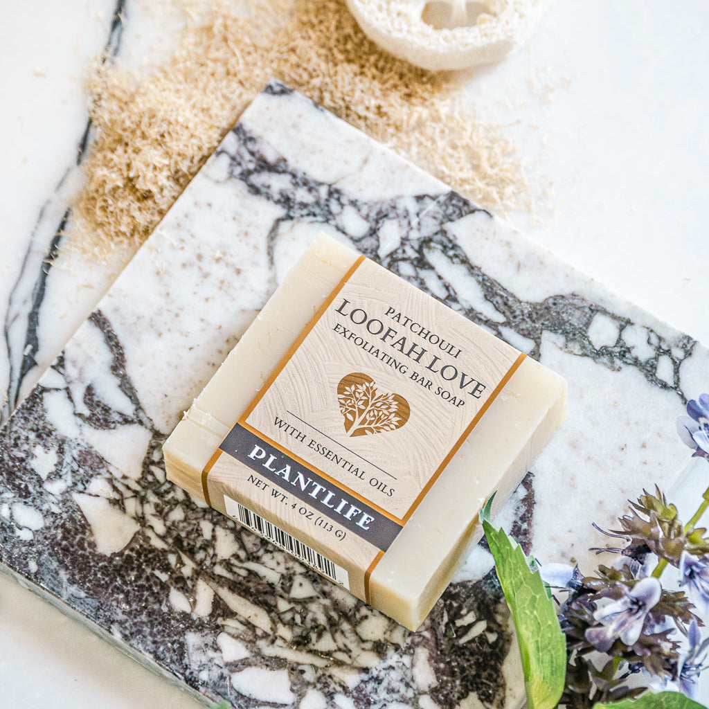 Bar of soap with packaging on a marble surface with herbs and flowers.