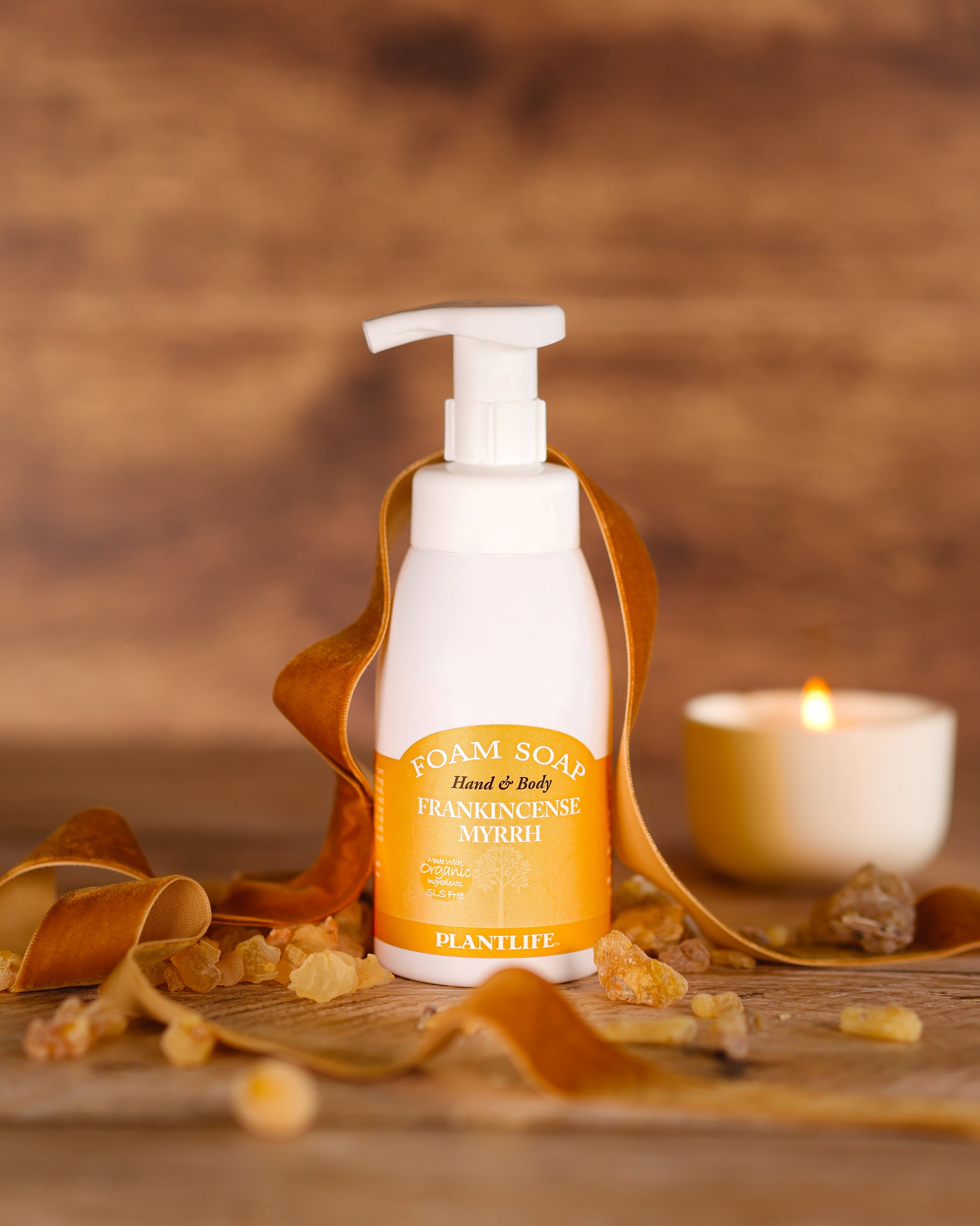 Foam soap bottle with frankincense myrrh on a wooden surface with a candle in the background
