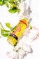 Yellow bottle of plant-based body oil with green leaves and white flowers on a white background