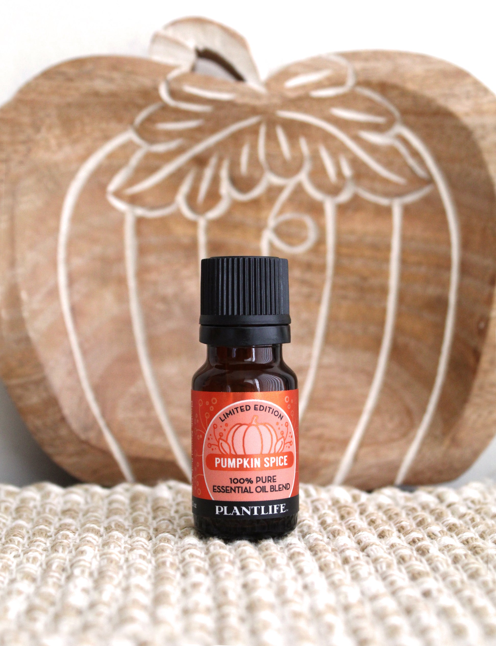 Bottle of Plantlife Pumpkin Spice essential oil blend with a decorative wooden pumpkin in the background.