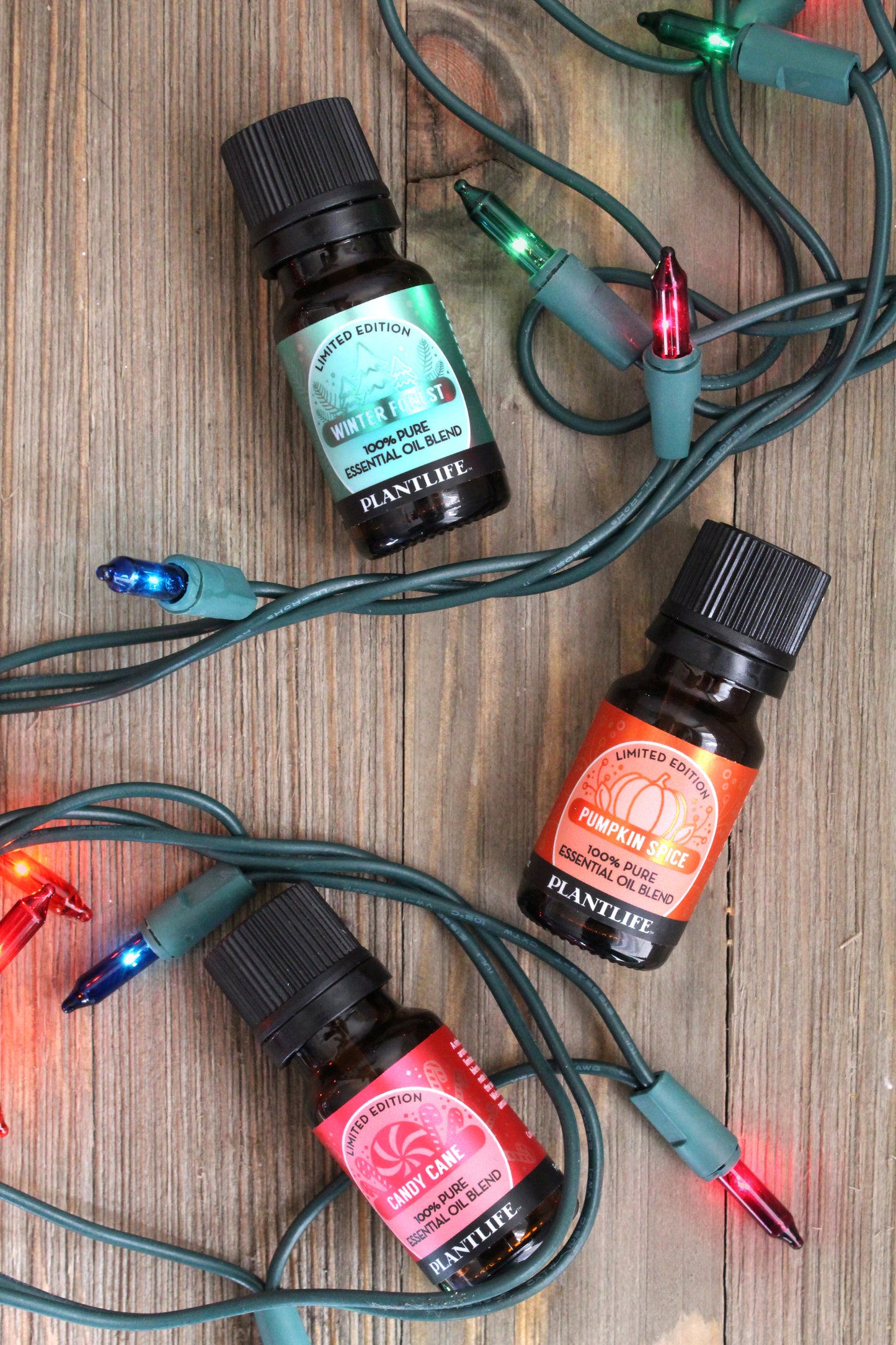 Three essential oil bottles with colorful Christmas lights on a wooden surface