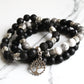 Stack of black, white, and gray beaded bracelets with tree of life charm on a marble surface