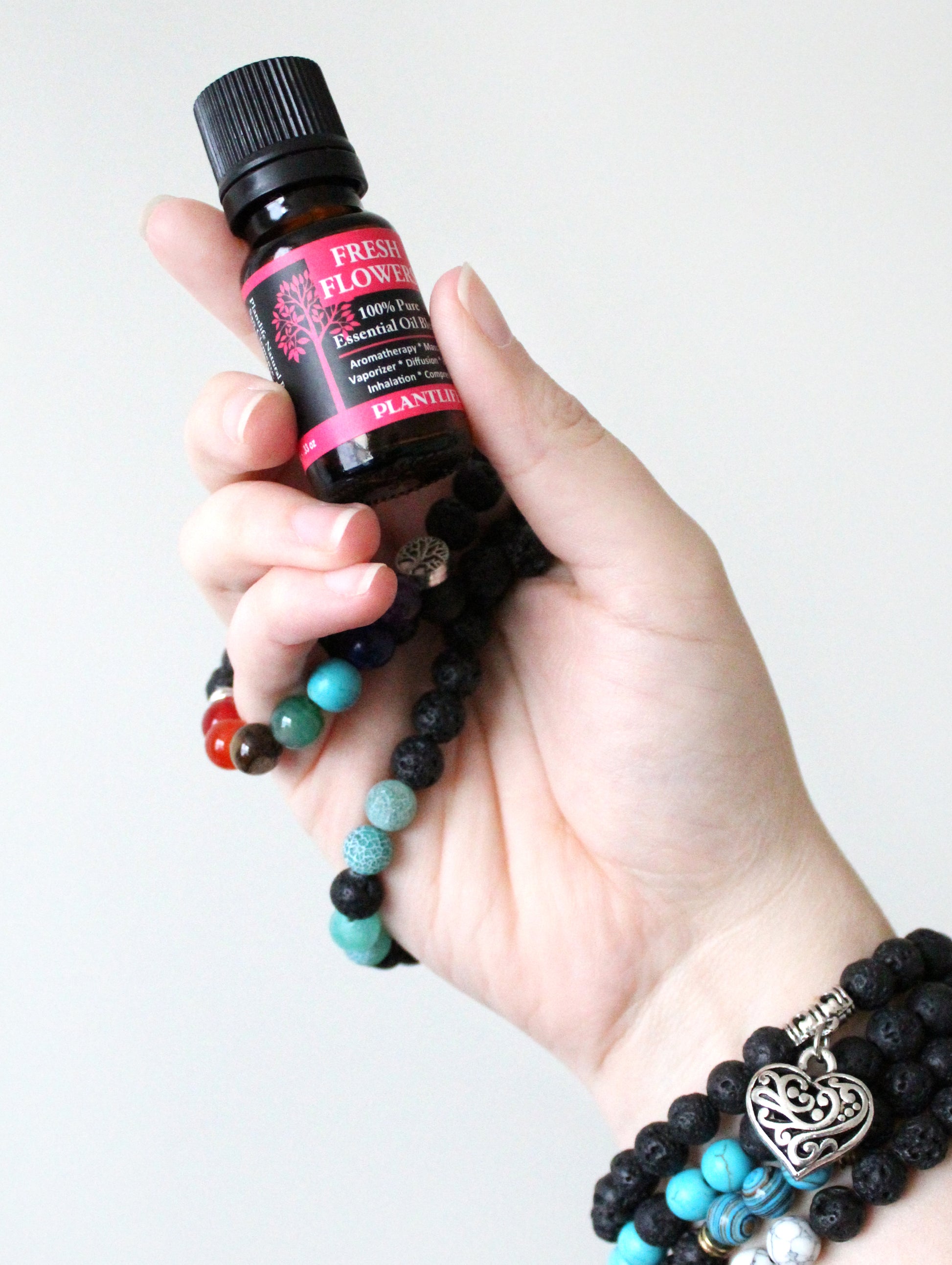 Hand holding a bottle of essential oil with multiple aromatherapy bracelets on a white background