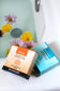 Two Plantlife bath salts packets on a white surface with flowers in the background