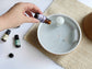 Hand pouring essential oil into a diffuser on a white surface with a textured mat.