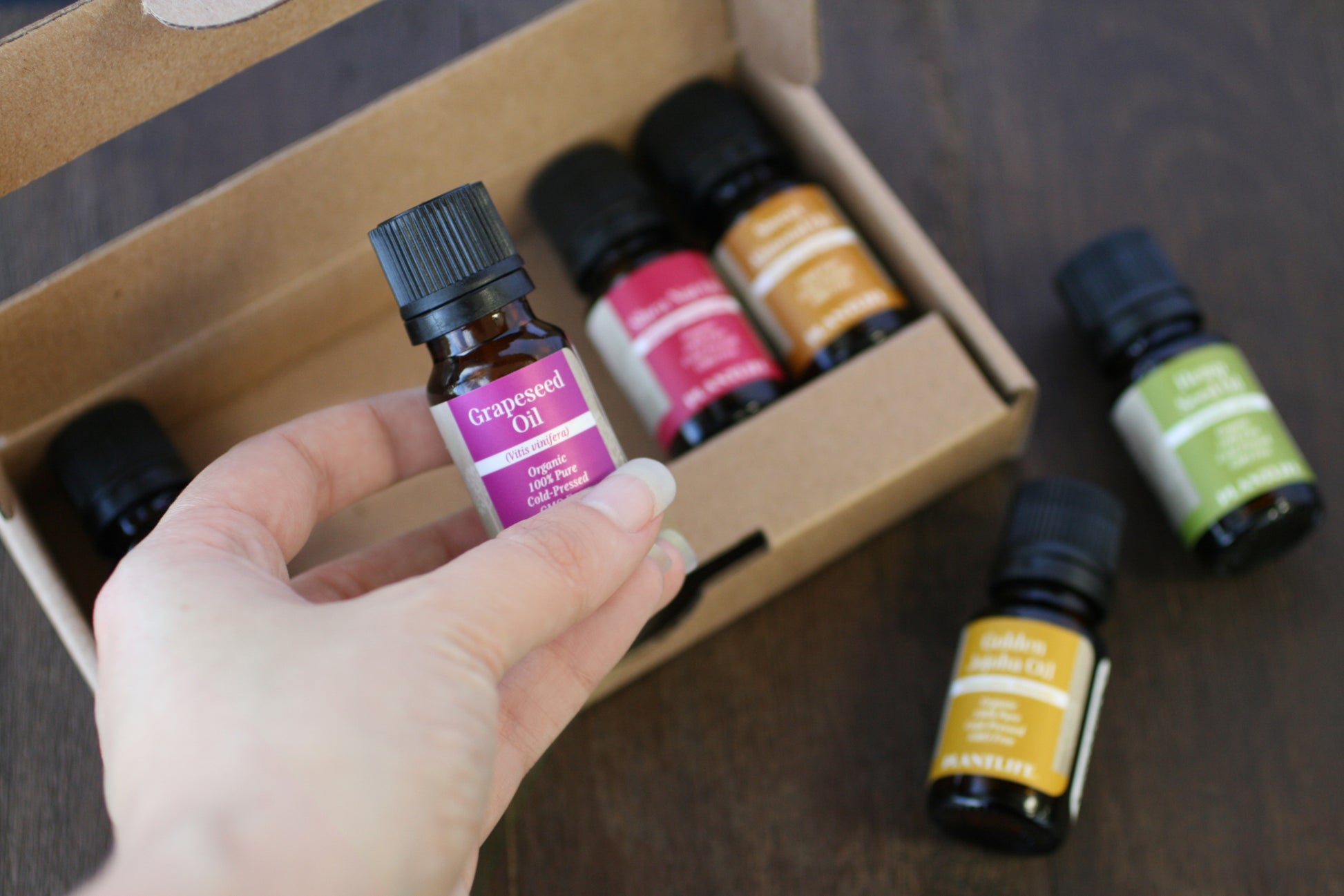 Hand holding a bottle of grapeseed oil with other essential oil bottles in the background.