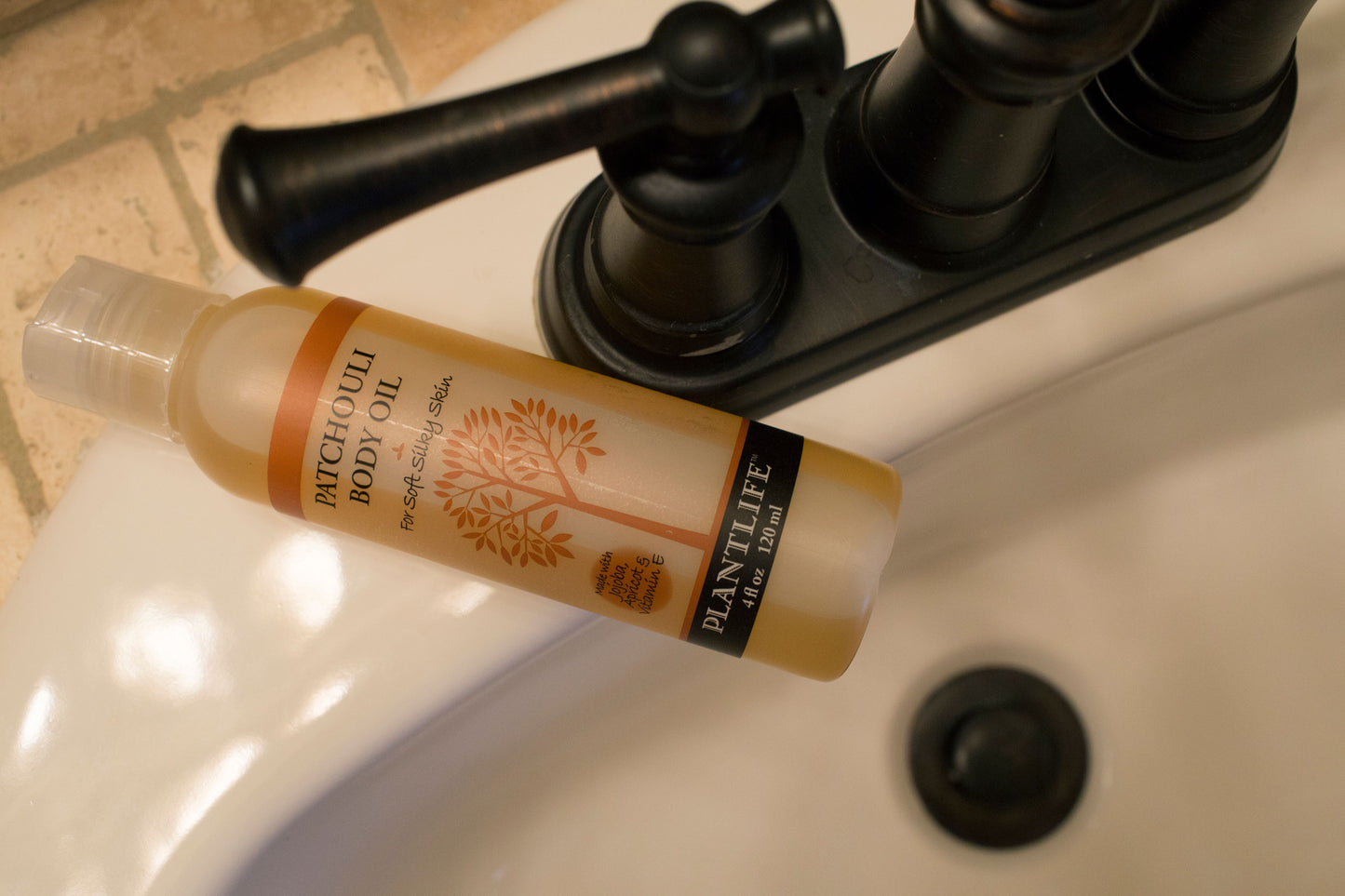 Bottle of Patchouli Body Oil on a sink with a black faucet