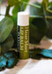 A tube of Hemp Mint Lip Balm by Plantife, standing upright on a marble-like surface with green leaves in the background.