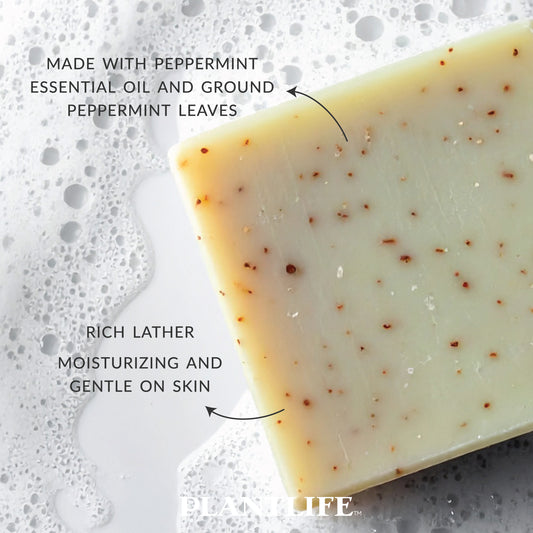 Close-up of Plantlife Peppermint Soap with visible peppermint leaf specks and foamy bubbles. Text reads “Made with peppermint essential oil and ground peppermint leaves” and “Rich lather moisturizing and gentle on skin.” Refreshing, cooling soap handcrafted with natural essential oils for clean, soft skin.