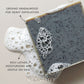 Close-up of a dark gray Plantlife soap bar with visible exfoliating particles resting in foamy water. Text on the image highlights “Ground sandalwood for heavy exfoliation” and “Rich lather, moisturizing and gentle on skin.”