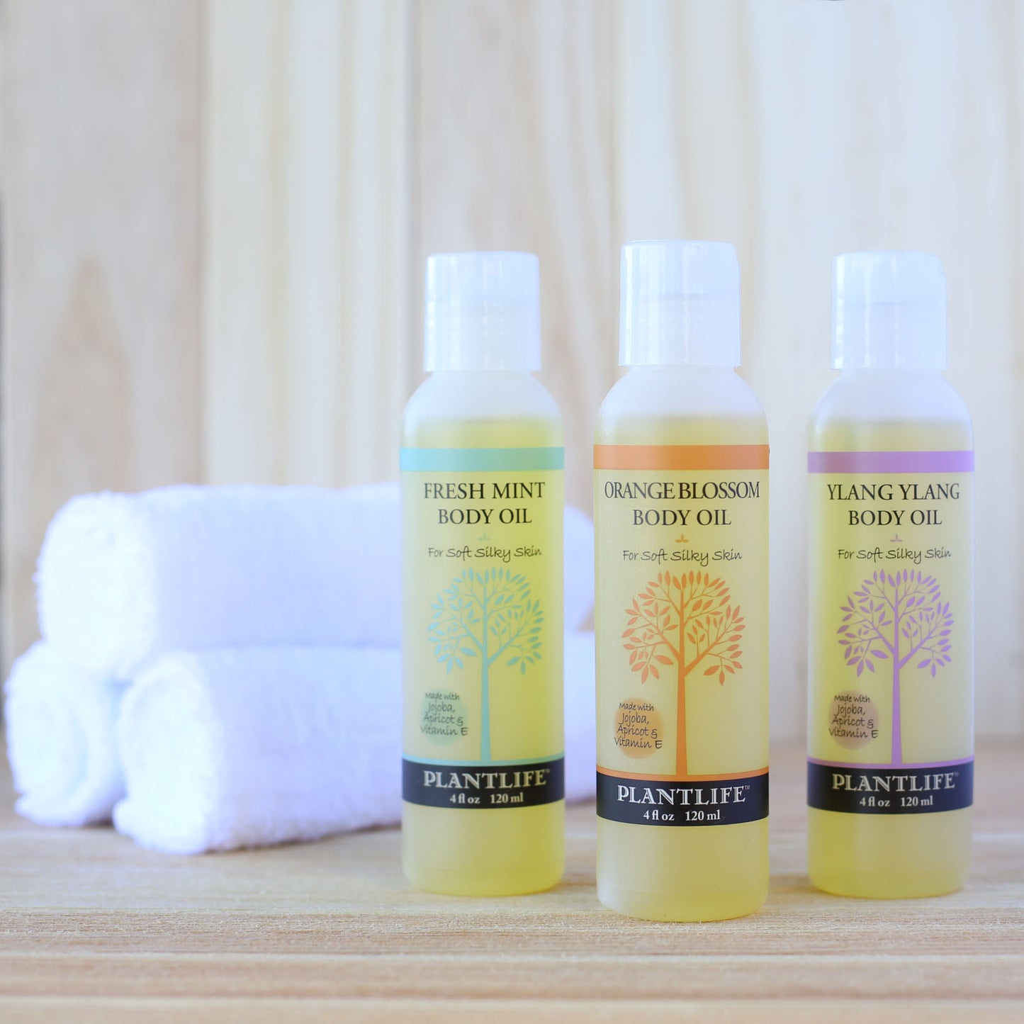 Three bottles of Plantlife body oils on a wooden surface with a white towel in the background.