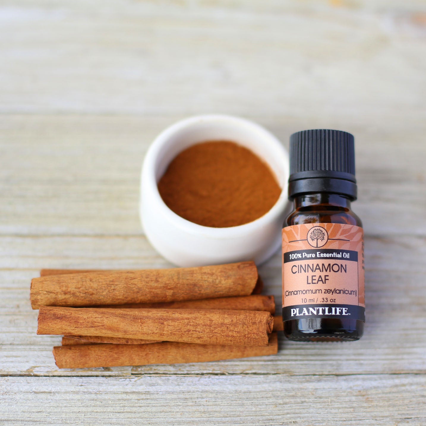 Cinnamon essential oil bottle, cinnamon sticks, and ground cinnamon on a wooden surface