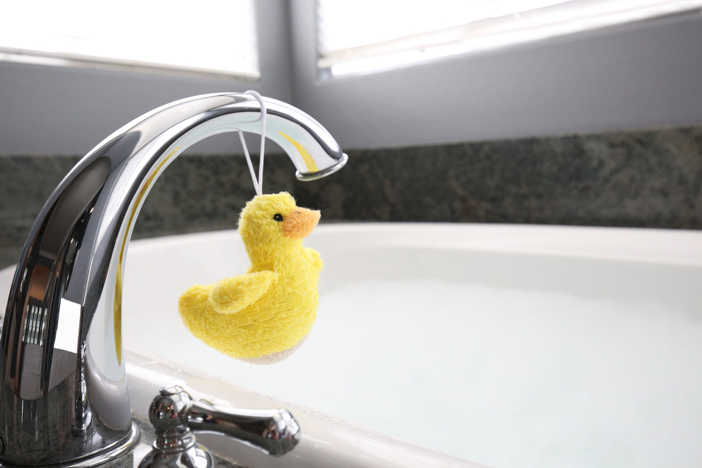 Yellow duck Ramie hanging from a silver faucet in a bathroom